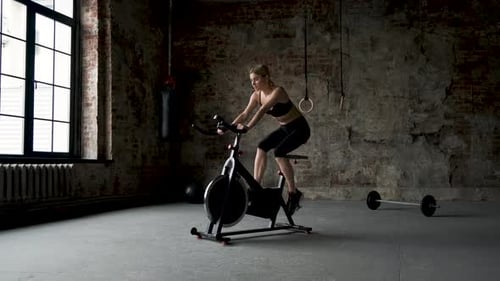 Young active woman spinning air bike in gym. Female training on air bike in slow motion.