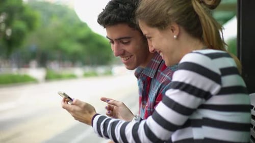Young Couple Using Smart Phone at Bus Stop