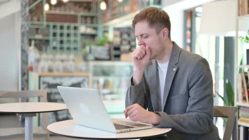 Man Coughing at Laptop in Coffee Shop