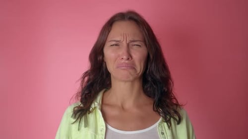 Young Attractive Girl Desperately Crying on a Pink Wall Background
