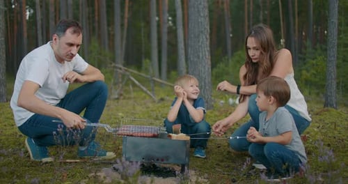 Married Pair with Two Little Sons Are Resting at Nature, Grilling Sausages in Forest, Family Picnic