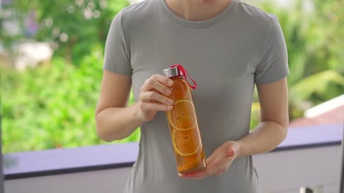 Une femme tient une bouteille de boisson au kombucha dans ses mains qui a une saveur d'orange