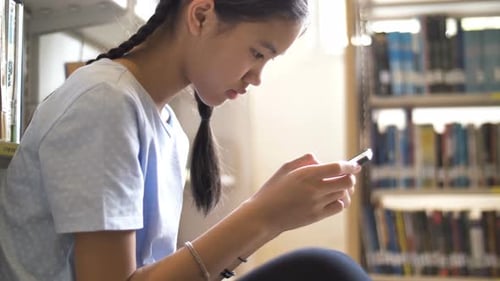 Asian teenager student using smart phone in school library.