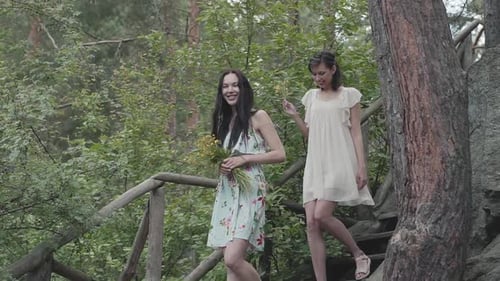 Two Young Women in Short Dresses with Flowers Go Down the Stairs and Looking at Amazing Forest, Trees