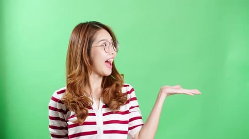 Junge Frau zeigt im Studio auf ein Objekt, das mit Chroma-Key grafisch eingegeben werden soll