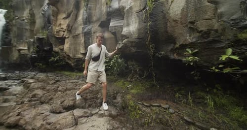 Handheld Close Up Going Into Wide View of a Young Male Explorer Walking Down a Rocky Cliff Away From