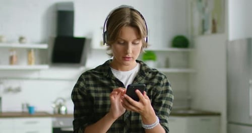 Woman Using Smartphone in a Kitchen with Headphones