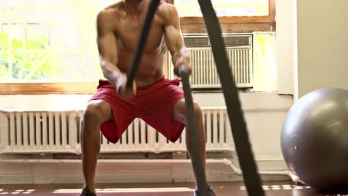 Muscular Man Exercising with Battle Ropes in Gym