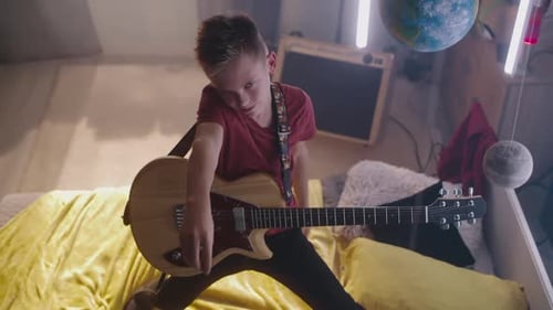 Teen Boy Playing Electric Guitar in Bedroom