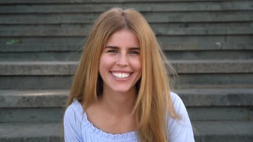 Happy young woman smiling into the camera while sitting on urban stairs