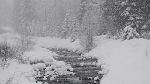 Heavy snow falls over a snow lined river
