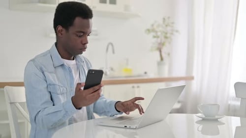 Young Adult Using Phone and Laptop at Table