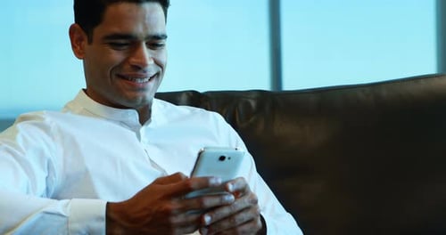 Man Smiling While Using Mobile Phone Indoors