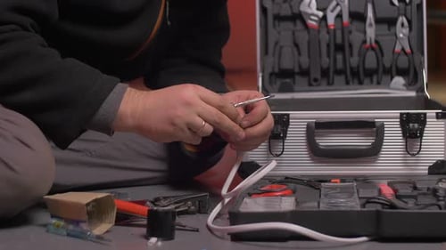 Man repairs white electrical cable with screwdriver