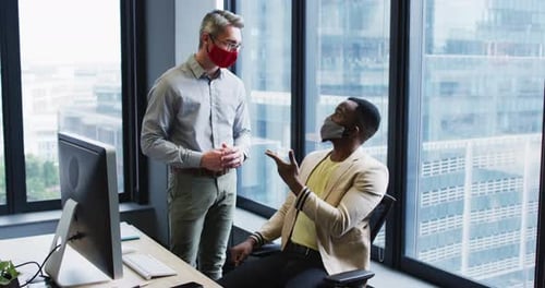 Diverse male office colleagues wearing face masks discussing at modern office