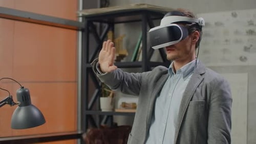 Young Male Engineer in Office in Virtual Reality Helmet with Hands Makes Movements Imitating the