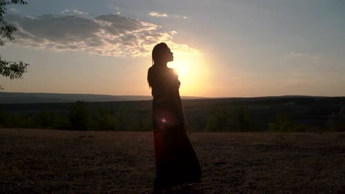 Woman Silhouetted Against Golden Sunset in Field