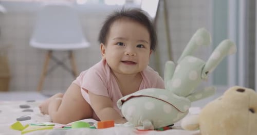 Smiling Baby Lying on Blanket Surrounded by Toys