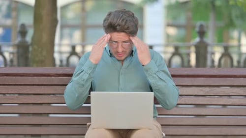 Man Using Laptop on Bench Rubbing Temples