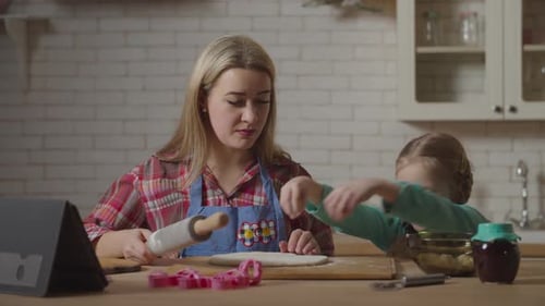 Hija feliz añadiendo harina a la masa durante la cocción