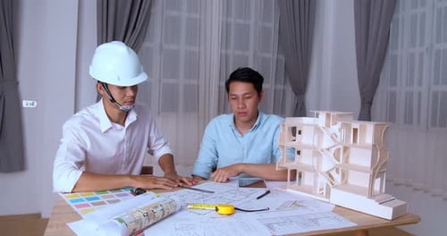 Two Asian Male Architects In Office Discussing Construction Project