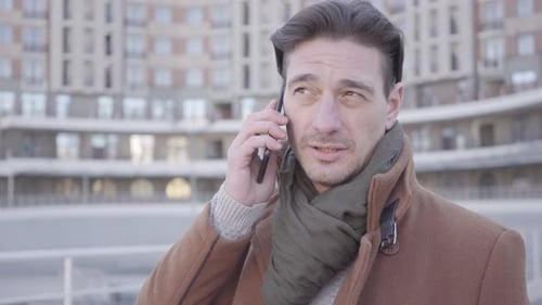 Portrait of Handsome Confident Man in Brown Coat Standing in the City Street Talking By Mobile Phone