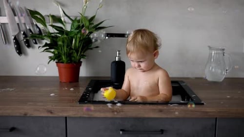 Child Bathes with Duck Toy in Kitchen Sink