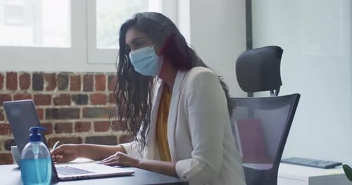 Woman wearing face mask taking notes in office
