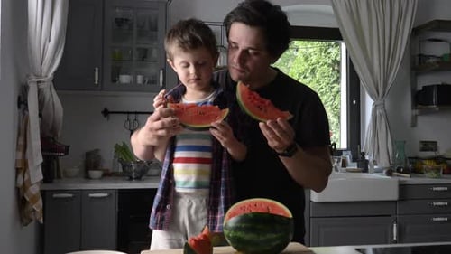 Father and Son Eat Watermelon in Kitchen
