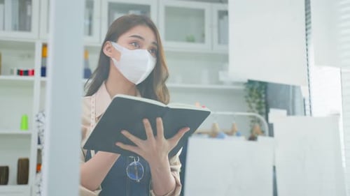 Asian beautiful tailor dressmaker woman wear mask, checking new fashionable handmade in atelier.