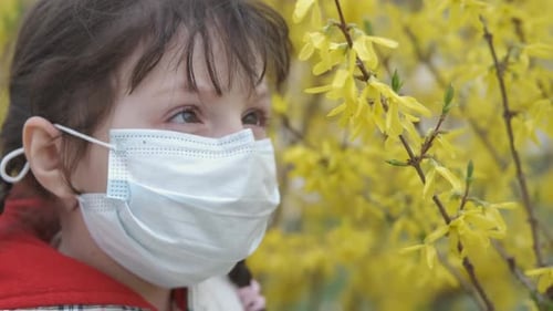 Child Wearing Mask near Yellow Spring Flowers