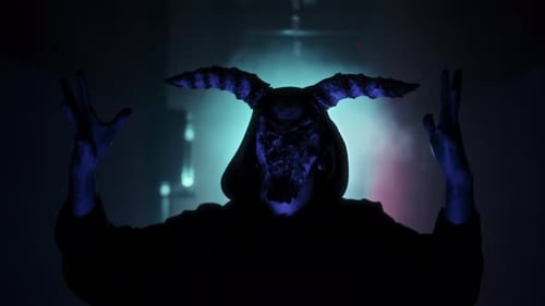 Demonic Masked Figure Raises Arms in Dark Room