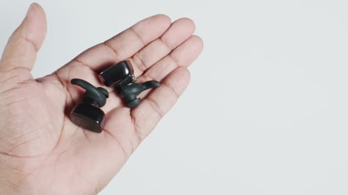 Hand Holding Two Black Wireless Earbuds