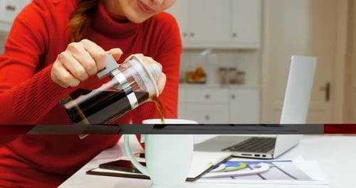 Woman Pours Coffee at Kitchen Table with Laptop