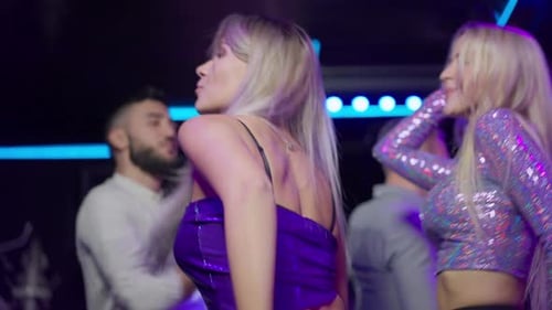 Seitenansicht einer schlanken, glücklichen jungen Frau, die im Nachtclub tanzt, singt und Spaß mit einer Gruppe von Freunden hat