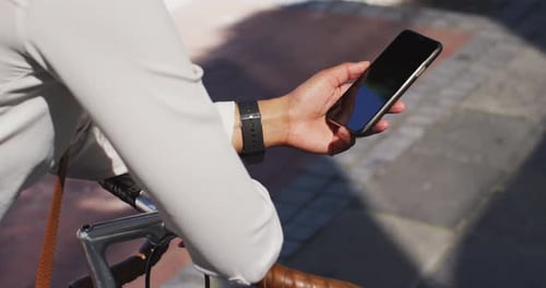 Midsection of african american woman using smartphone leaning on bike in street