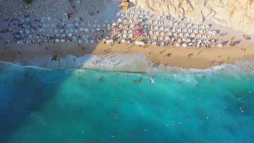 Menschen schwimmen auf hellblauem Meer am weißen Sandstrand in der Nähe des felsigen Berghangs