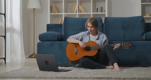 Woman Plays Guitar at Home With Laptop