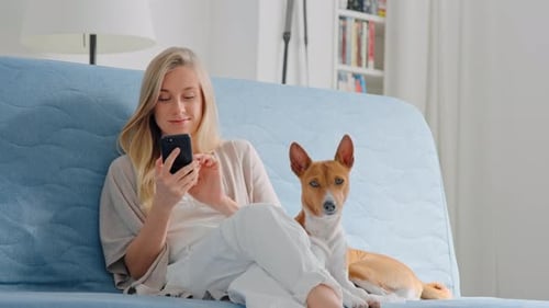Woman Using Phone with Dog on Couch Indoors