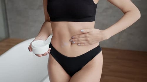 Unerkennbare Frau, die Creme auf den Bauch aufträgt und den Körper im Badezimmer befeuchtet