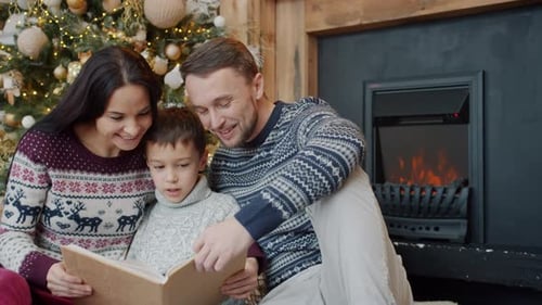 Family Reading Book near Christmas Tree and Fireplace