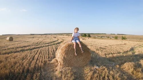 Little Girl in a Field with Hay Jump at Sunset. Girl Near a Hay Bale in the Countryside.