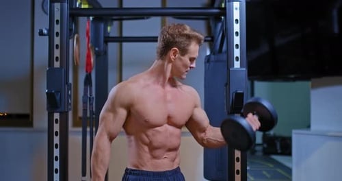 Professional Athlete Shakes the Biceps of the Arms with the Help of Dumbbells, Raises the Dumbbells