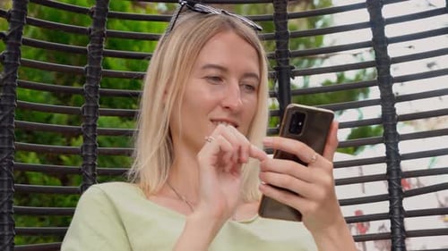 Woman Using Smartphone in Hanging Chair Outdoors