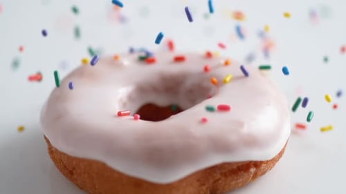 Bonbonschokolade auf gefrosteten Donut streuen. Zeitlupe.