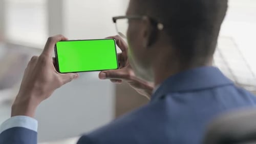 Man Looks at Green Screen Smartphone in Office