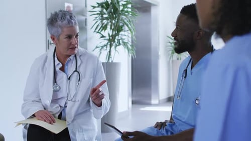 Caucasian female senior doctor discussing with diverse male colleagues at hospital staff meeting