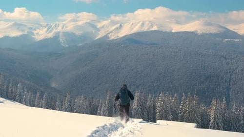 Successful Hiker with Backpack Walking on Snowy Mountain Hillside on Cold Winter Day