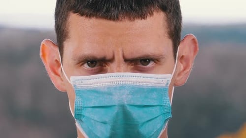 Young Man in a Medical Protective Face Mask Looking at the Camera on the Street Background