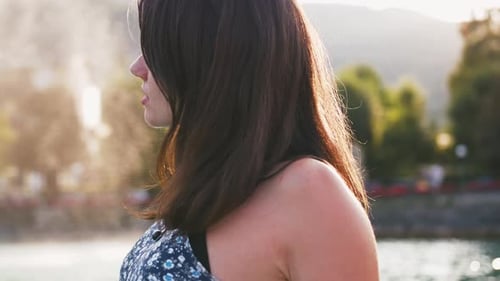 Portrait of Young Woman in Dress Sitting at the Edge of Wooden Pier at Lake in Mountains Enjoying